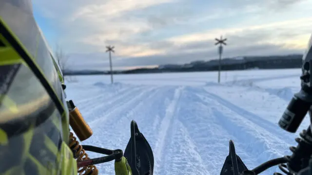 Skoterled över ett snötäckt fält i kvällsljus, sett från skotern